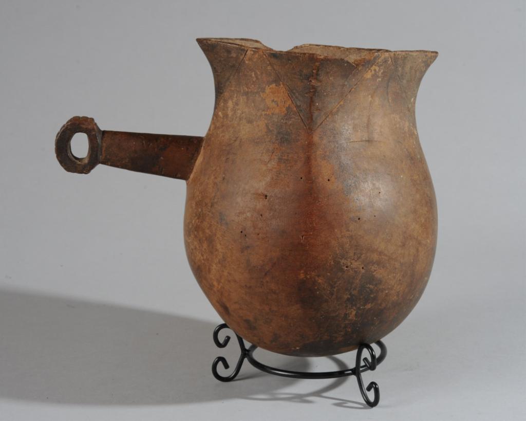 Ethiopian Wooden Vessel: Thin-walled rounded wooden pot with flaring rim shaped for pouring, and with long handle. Incised triangular design at rim. Shows age and use. Minor old insect damage, losses, cracks. Includes metal b