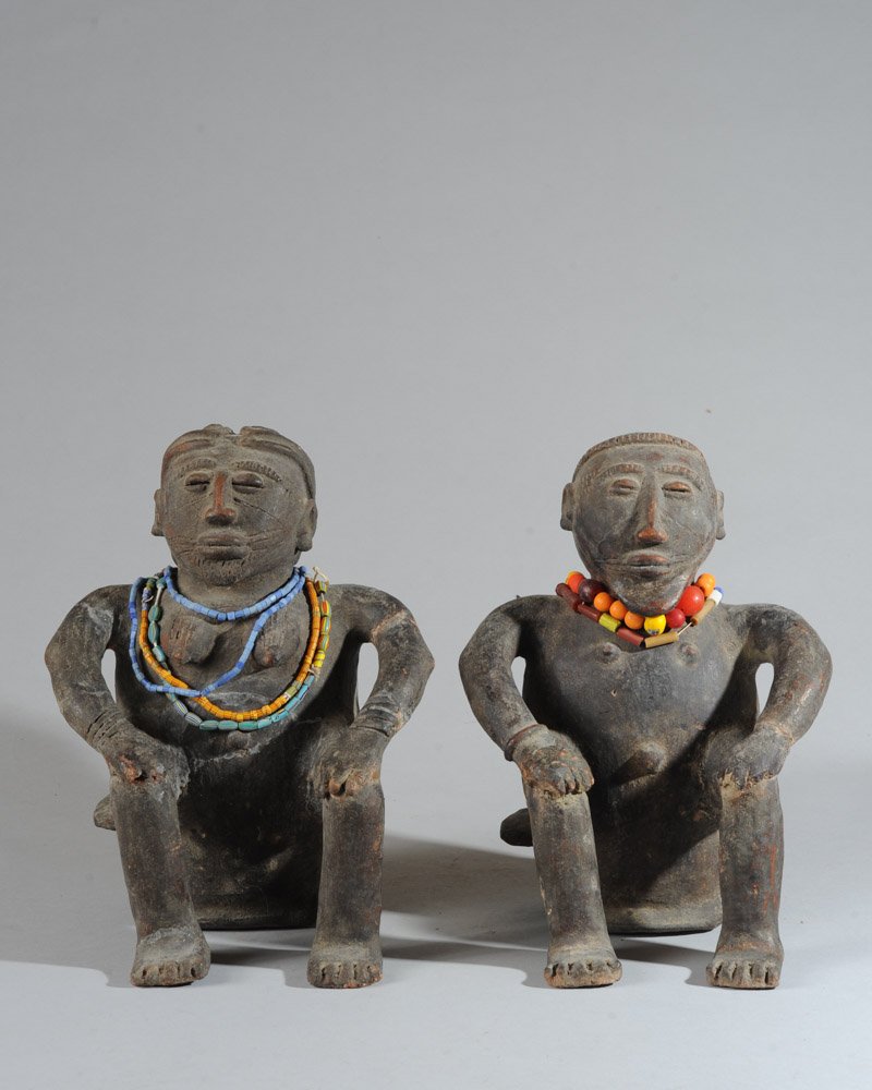 Pair of Bobo Seated Terracotta Figures: Blackened terracotta figures, probably male and female, seated on stools with heads high and hands on knees in attitudes of authority, the female with lobed coiffure, the male with knobbed cap, both h