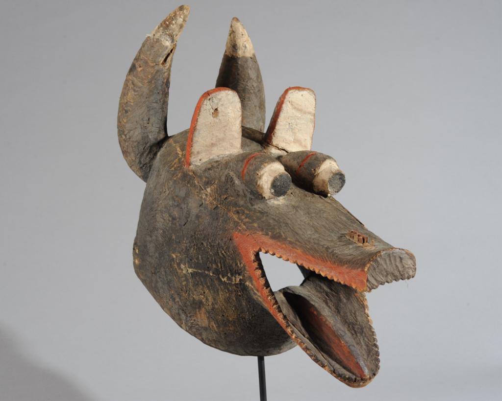 Mumuye Animal Mask, Nigeria: Vivacious zoomorphic mask with horns, upright ears, protruding eyes, and a long snout with a wide open toothy mouth. Carved wood and pigments. Includes custom gallery stand. Mask, approx. 19" L x 14" 