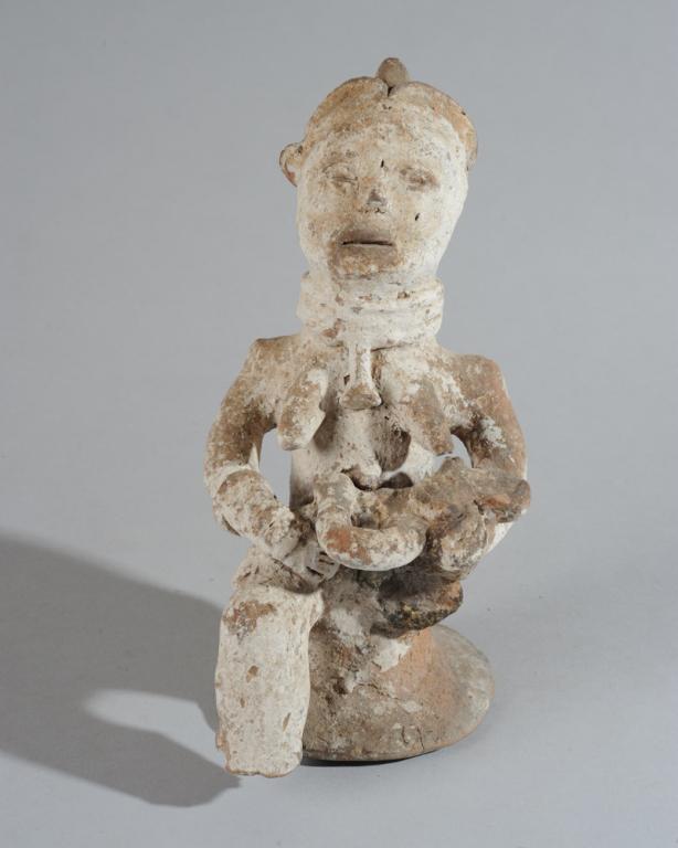 Igbo Terracotta Maternity Figure, Nigeria: Seated figure of a mother nursing an infant, one arm cradling his head, the other tucked around his body, the composition conveying tenderness, nurture and protection. Terracotta, with worn, whitened 