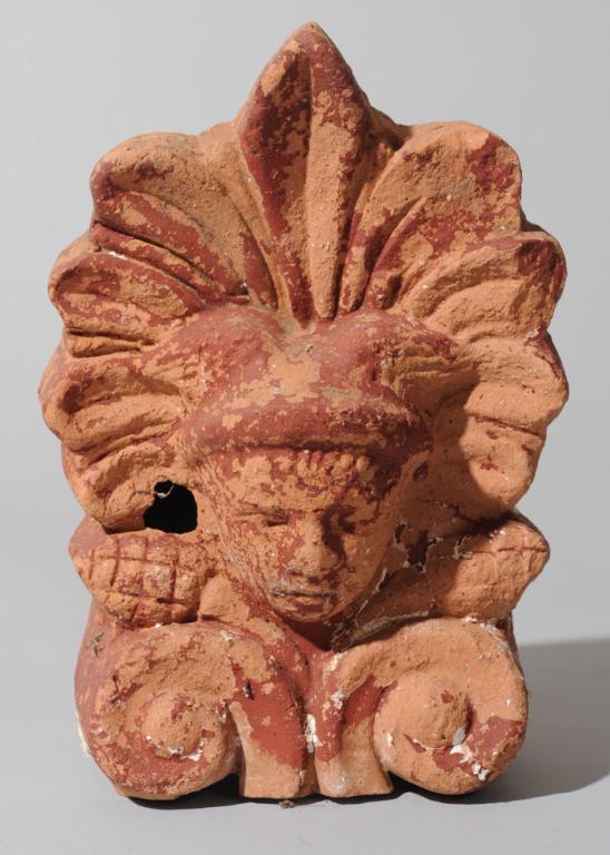 Roman Terracotta Antefix: With the winged head of Mercury, acanthus leaf rising behind and pine cones on either side above two scrolling elements. With traces of old red pigment and white gesso-like material. Untested but like