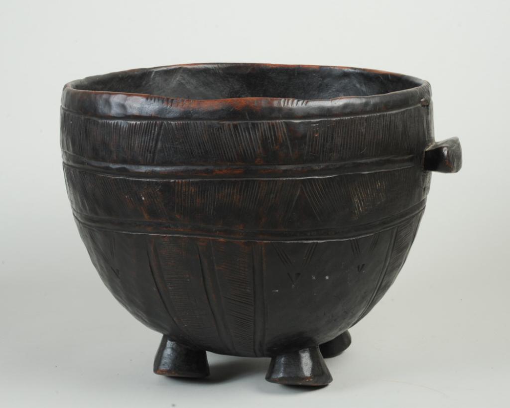 Large Fulani Footed Wooden Pot: Carved wood with incised geometric decoration, on four canted feet, with side handle, old staple repair. Fulani people, West Africa. Approx. 10" H x 12 1/2" D. Provenance: Estate of Thomas McNemar, (1