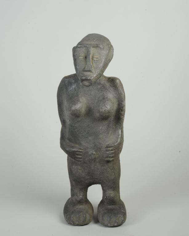 Standing Earthen Female Figure, Africa: Central or West African figure made of dense, solid, heavy black clay. Elongated head and jaw, with large ears, embedded cowrie shell eyes, standing with arms held against the body, hands cupping the 