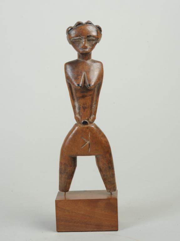 Guro or Baule Slingshot, Ivory Coast: Figural catapult, of feminine form, with four-lobed plaited coiffure, prominent breasts and narrow waist. Golden brown wood embellished with black pigment. Warm, oily patina. On custom gallery base. S