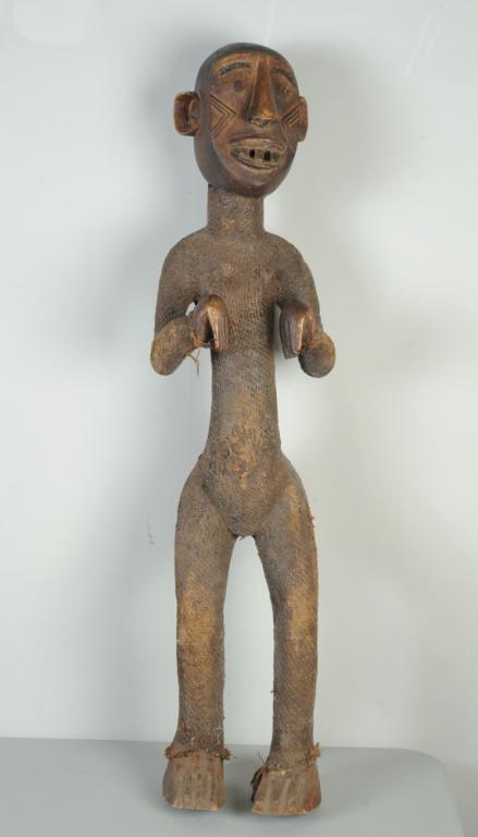 African Large Standing Figure: Large standing figure with monkey figures including protruding round ears, large toothy mouth, with relief carved chevron marks to cheeks, the arms held apart from the body, bent at the elbows and wri