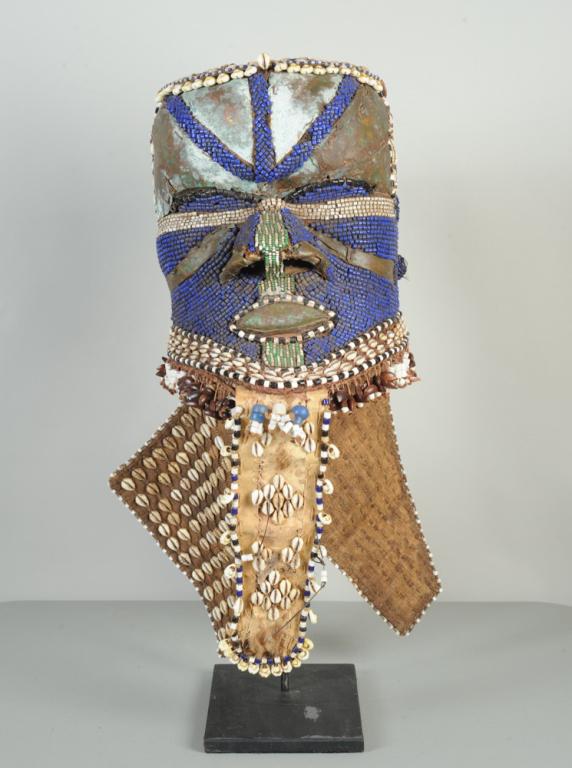 Kuba Bwoom Mask, D. R. Congo: Helmet mask with sheet copper, beads, shells, seed pods, fabric and animal hide. Such masks are used in dances which tell of the founding of the Kuba kingdom. On custom gallery stand. Some losses. Mas