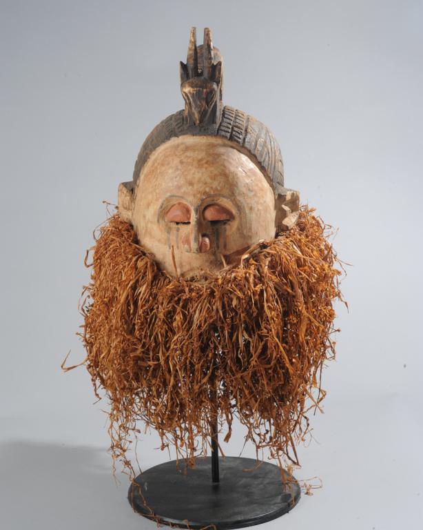 Suku 'Hemba' Style Helmet Mask, D. R. Congo: Helmet mask of the type associated with initation rites, with an antelope perched atop a head with elaborately incised coiffure, the whitened face with reddened eyes and nose and tear marks on the che