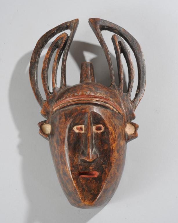 African Mask: Small hardwood mask with a human face surmounted by large openwork horns, the flat facial plane dominated by a prominent nose, with small eyes and mouth embellished with red and white pigment. Tribe a