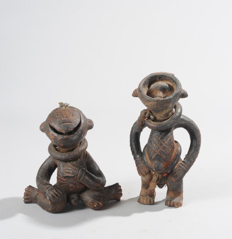Unusual African Terracotta Figures: Two figures; one a seated male figure of blackened clay, looking upwards; the face lifts like a lid to reveal a cavity with another face inside; residue of organic material in this cavity and in the e
