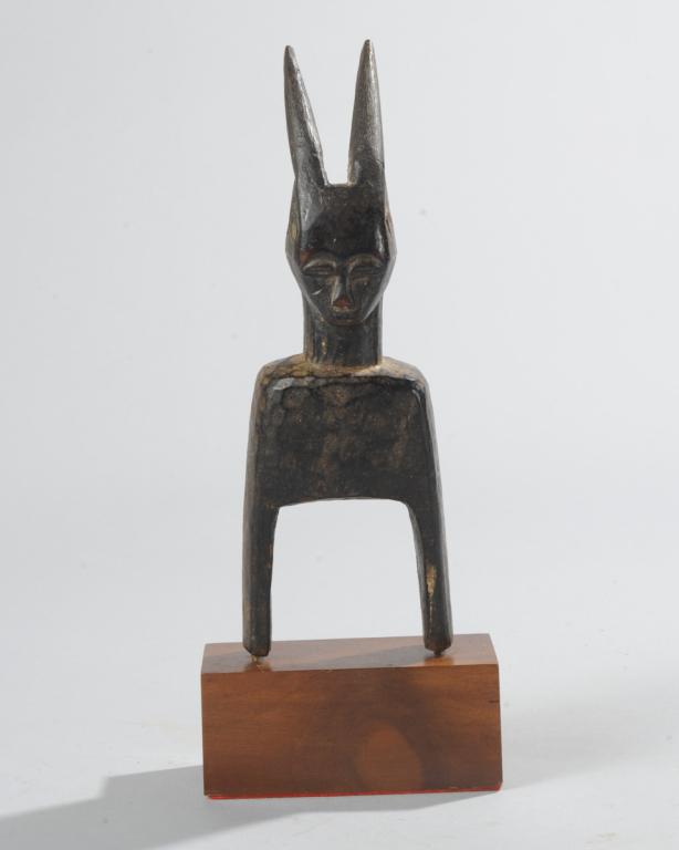 West African Heddle Pulley: With backward-curving horns, human face. Ivory Coast. On custom gallery stand. Total height approx. 10". Provenance: Estate of Thomas McNemar, (1931-2020.) McNemar lived and collected throughout Centr