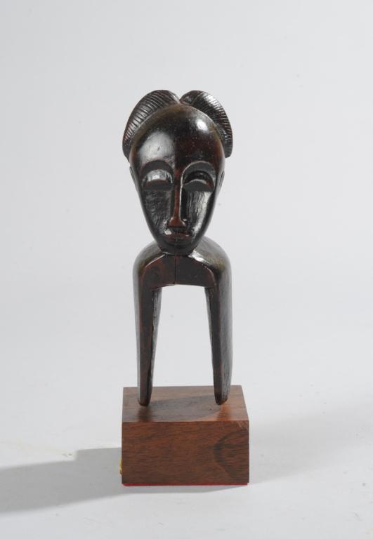 Baule Heddle Pulley: Anthropomorphic finial with large rounded forehead above arched brows and half-moon eyes, with horns or lobed coiffure. Ivory Coast. On custom gallery stand. Total height approx. 8 1/2". Provenance: E