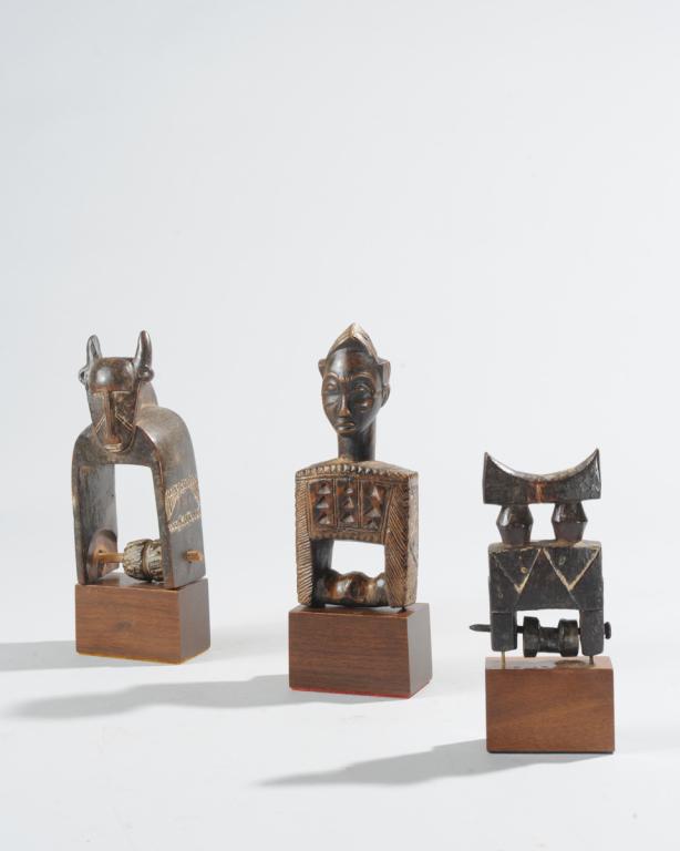 Three West African Heddle Pulleys: To include a finely carved anthropomorphic Baule pulley, a horned zoomorphic pulley--likely Jimini / Djimini, and a third pulley of abstract form. All probably Ivory Coast. All on custom gallery stand