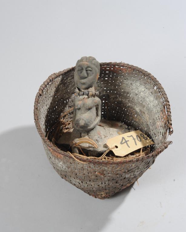 African Fetish / Shrine Basket: Woven basket containing a small carved figure of a kneeling pregnant woman, the figure embedded in some material (appears to have once been fixed in the material and now parts of the material are brok