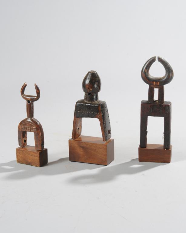 Three West African Heddle Pulleys: Two having finials with curved horns, the third with what appears to be an abstract human face on a bud shaped finial above chip carved neck and lower portion. All with custom gallery bases. Tallest, 