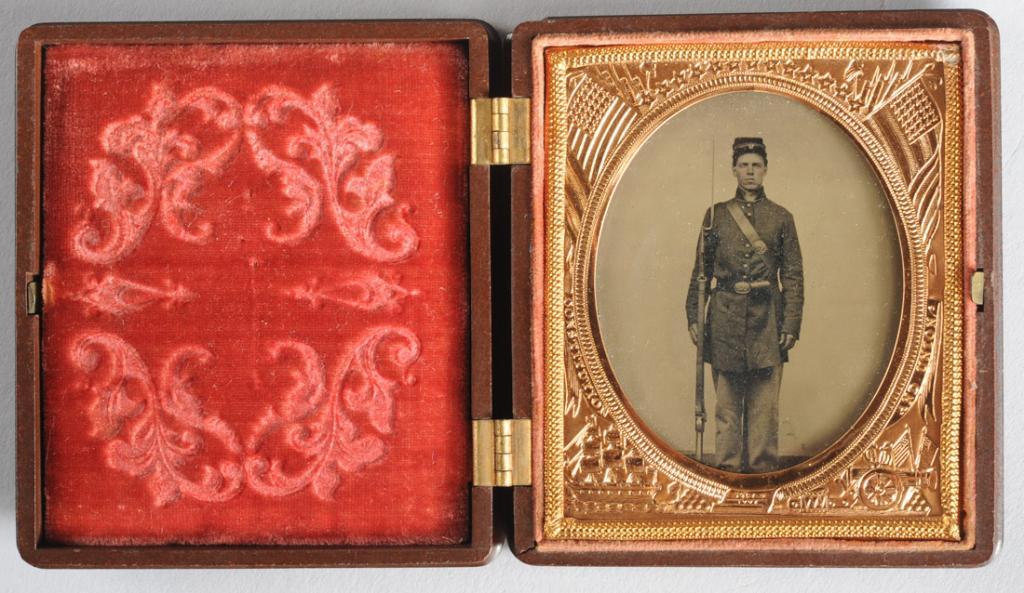 1/6 Pl. Tintype Armed Civil War Soldier Union Case: Clear and detailed 1/6 plate tintype of a handsome Union soldier at full length, in uniform and with rifle with bayonet. Advertisement printed on paper behind photo: "Genuine Union Case, Improved, Fin
