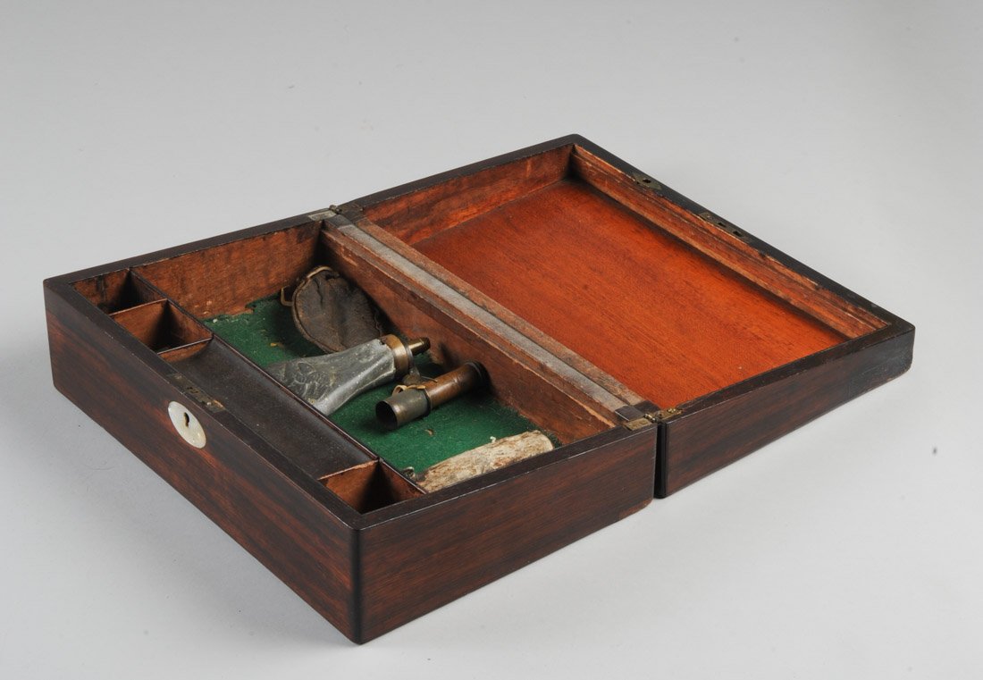 Mixed lot in Rosewood box: Small flask of tin, zinc or pewter, with brass cap, repousse eagle on shield on both sides, with dents, pin hole, approx. 5 1/2" L. Also, a small wood or horn flask, the surface flaking and damage to 