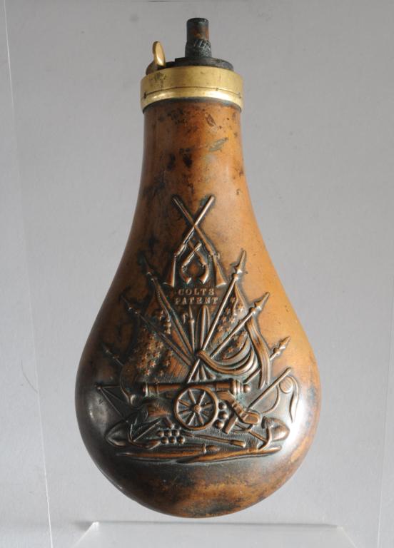 Medium Colts Patent Powder Flask: Colts Patent copper powder flask with brass lid and with repousse image on one side only of crossed arms, cannon, flags, anchor, spears. Working thumb plate. Minor small dents. Approx. 6 3/4". Provena