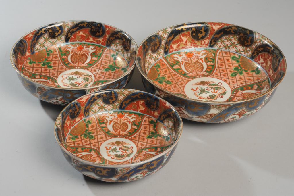 3 Japanese Imari Dragon Nesting Bowls, Meiji: Central orange dragons surrounded by floral elements in red, green, orange enamels and gilt and underglaze cobalt blue. Bases with Fuki Choshun mark. Meiji period. Approx. 10", 8 1/2", and 7 1/2" in d