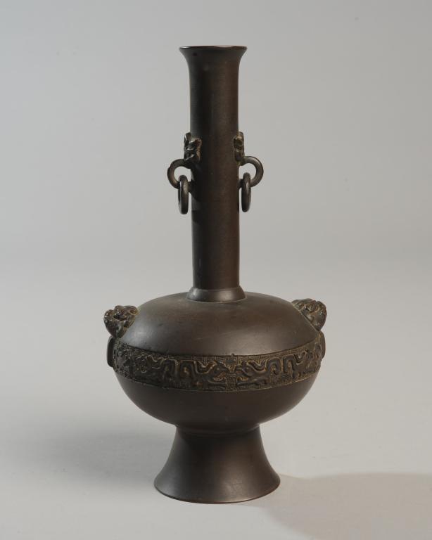 Japanese Bronze Vase in Chinese Style: In archaistic Chinese style, the slender neck with elephant masks and ring handles, the body with foo dog lug handles and a band of archaistic patterns in low relief. High pedestal foot. No marks. App