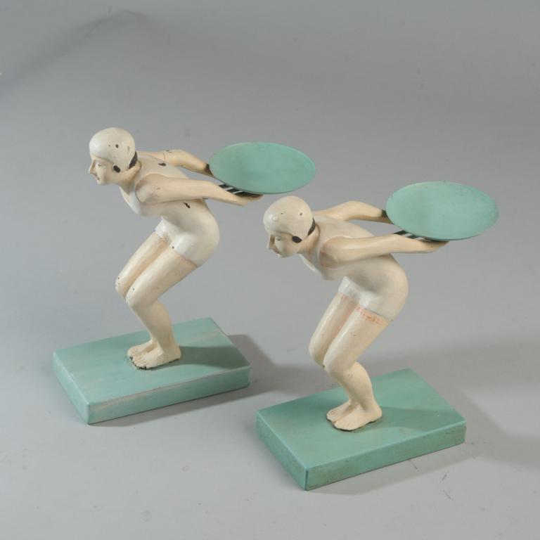 Pair Art Deco Female Swimmers Figures: Pair of composition figures of female swimmers in bathing suits and caps, posed as if about to dive, each holding a small metal tray behind her back. Possibly meant to support candles or hold calling 