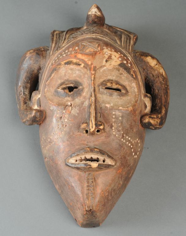 Ex-Thomas McNemar Chokwe Mask: Carved wood mask with coffee bean eyes set in round hollows, with slender nose and lips parted to show teeth, with typical markings to forehead and cheeks, zoomorphic headdress, curved horns or horn-s