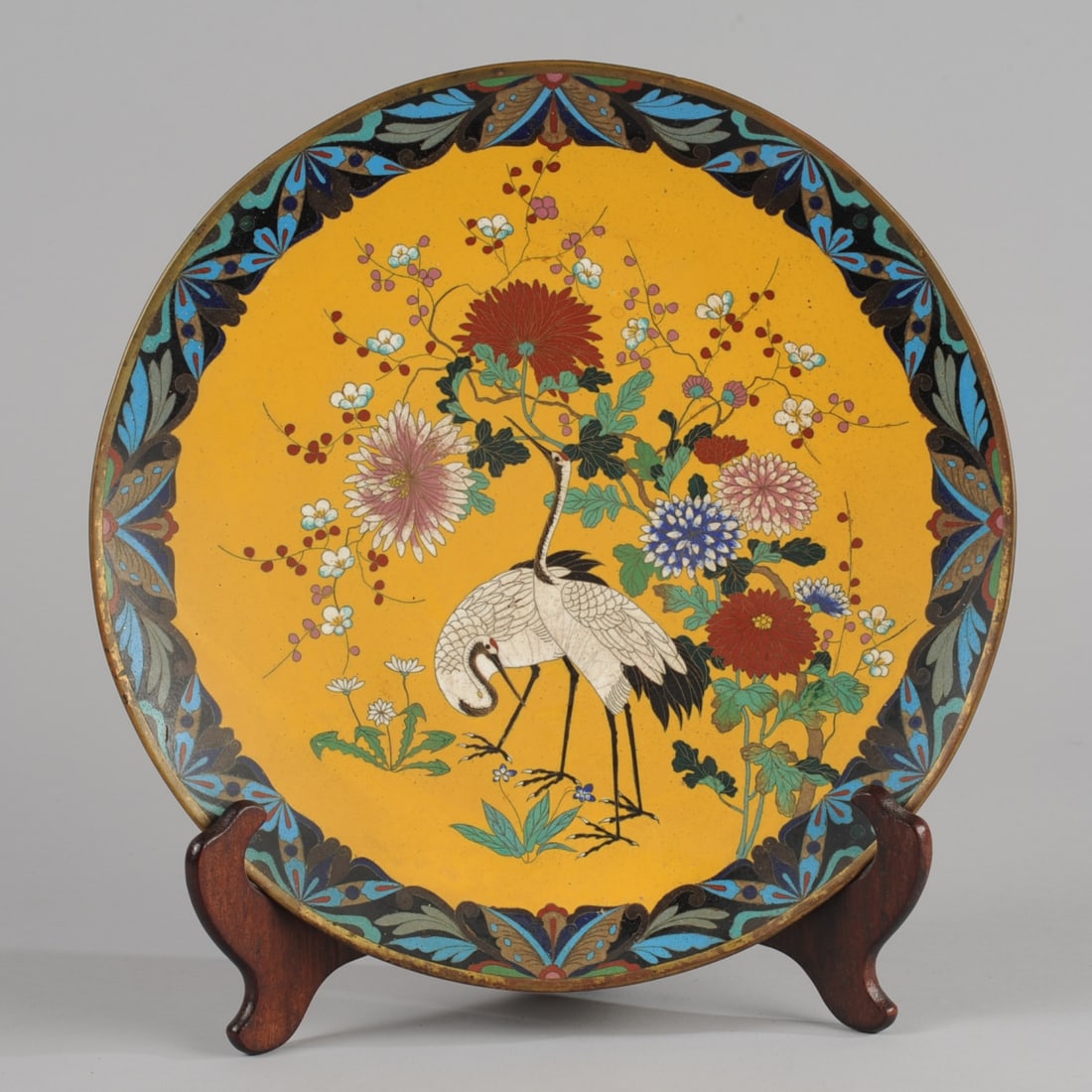 19th C. Japanese Cloisonne Charger: Richly colored Meiji charger with a central image of a pair of cranes among chrysanthemum and prunus on a saffron yellow ground, with a foliage and butterfly border in blues and greens with red and go