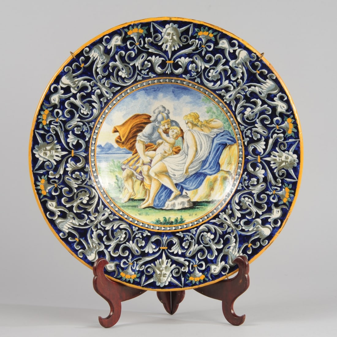 19th C. Italian Majolica Charger: The center with Renassiance style istoriato (story) decoration showing a landscape with a Roman soldier, a maiden or goddess, and a winged cupid. Broad border with griffins, masks, and foliate scrolli