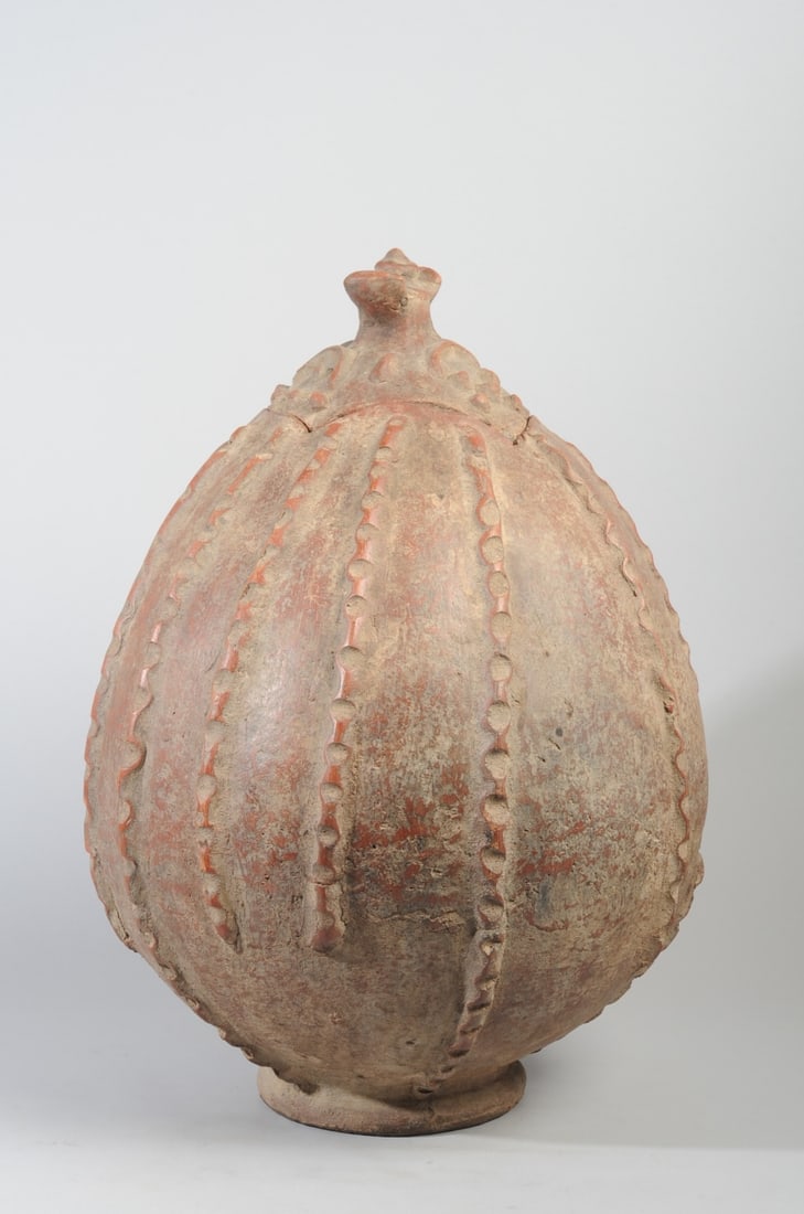 Lobi Pot, Burkina Faso: Ovoid terracotta pot on low foot, with vertical notched ridges, the lid with raised nubs and arched ridges and with decorative winged finial. Lobi artist, Burkina Faso. Approx. 22" H. Provenance: The 
