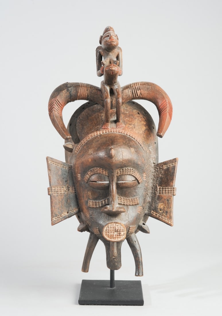 Senufo Kpelie Mask, Ivory Coast: Carved wood kpelie mask with pregnant female finial, details highlighted with red pigment and kaolin. Old insect damage. On custom gallery stand. Mask, approx. 7" W x 13 1/2" H x 4" D. Total height wi