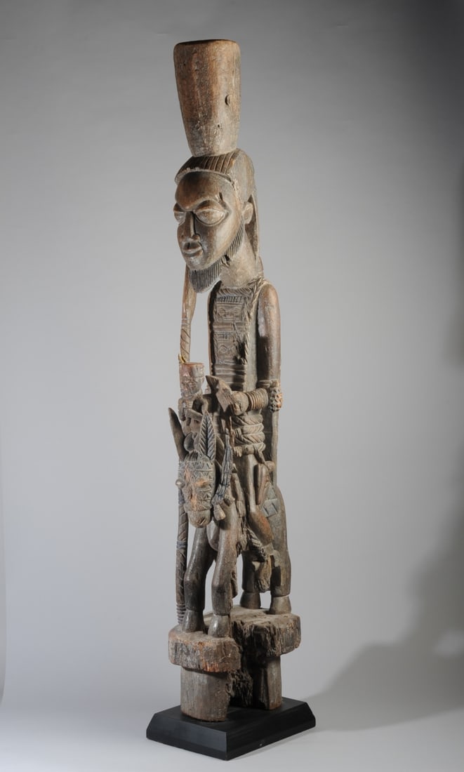 Yoruba Veranda Post: Elaborately carved equestrian figure architectural post, showing a warrior or royal figure astride a horse, a gun at his side, a spear grasped in one hand (spear damaged), the other hand holding a bri