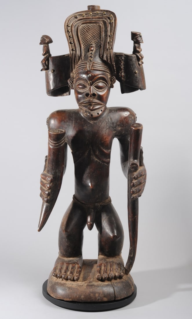 Chokwe Chibinda Ilunga Statue: Large, finely carved figure of Chokwe mythical hero and ideal chief, Chibinda Ilunga. The muscular figure is shown nude but for his elaborate headdress, upon which are perched two smaller figures. He 