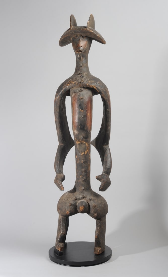 Mumuye Iagalagana Figure, Nigeria: Standing guardian figure with wide-brimmed headdress (or coiffure,) the face with staring, nub-like eyes, the nose just a slight rise in the surface of the face, notched along its length and with only