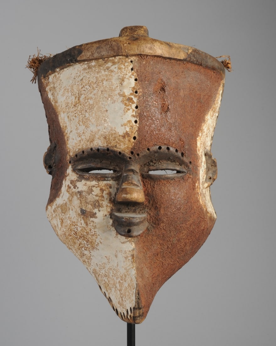 Tribal Mask, Gabon: Possibly Tsogo/ Mitsogo or Vuvi. Shield shaped face below flat-top head with cranial ridge. Face with white pigment on one side, dark reddish brown pigment on the other, with contrasting arcs of color