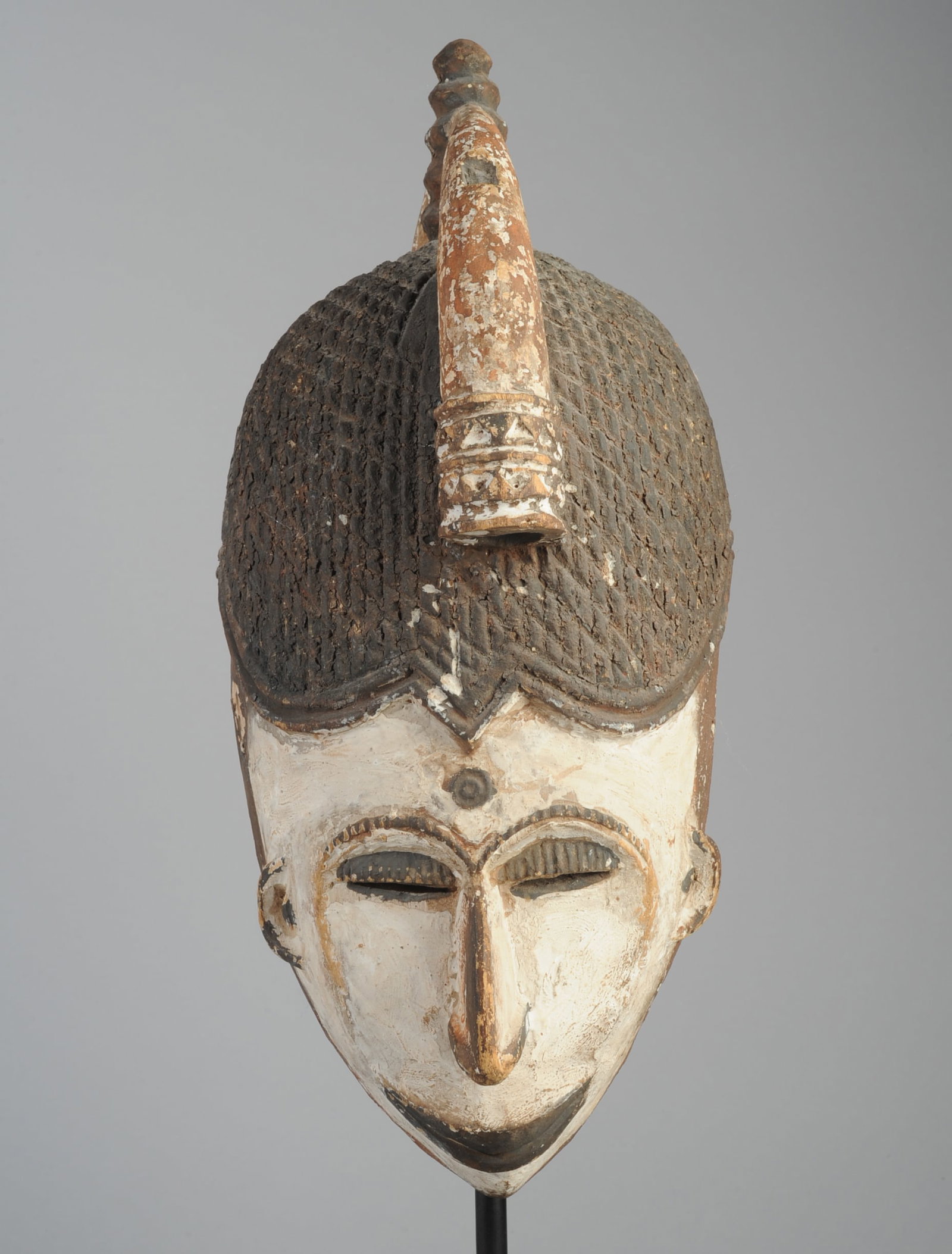 Igbo Agbogho Mmwo Mask, Nigeria: Igbo 'maiden spirit' helmet mask, the high coiffure and headdress with an upright central knob joining two tusk-like projections front and back. The heart-shaped face with downcast eyes, aquiline nose