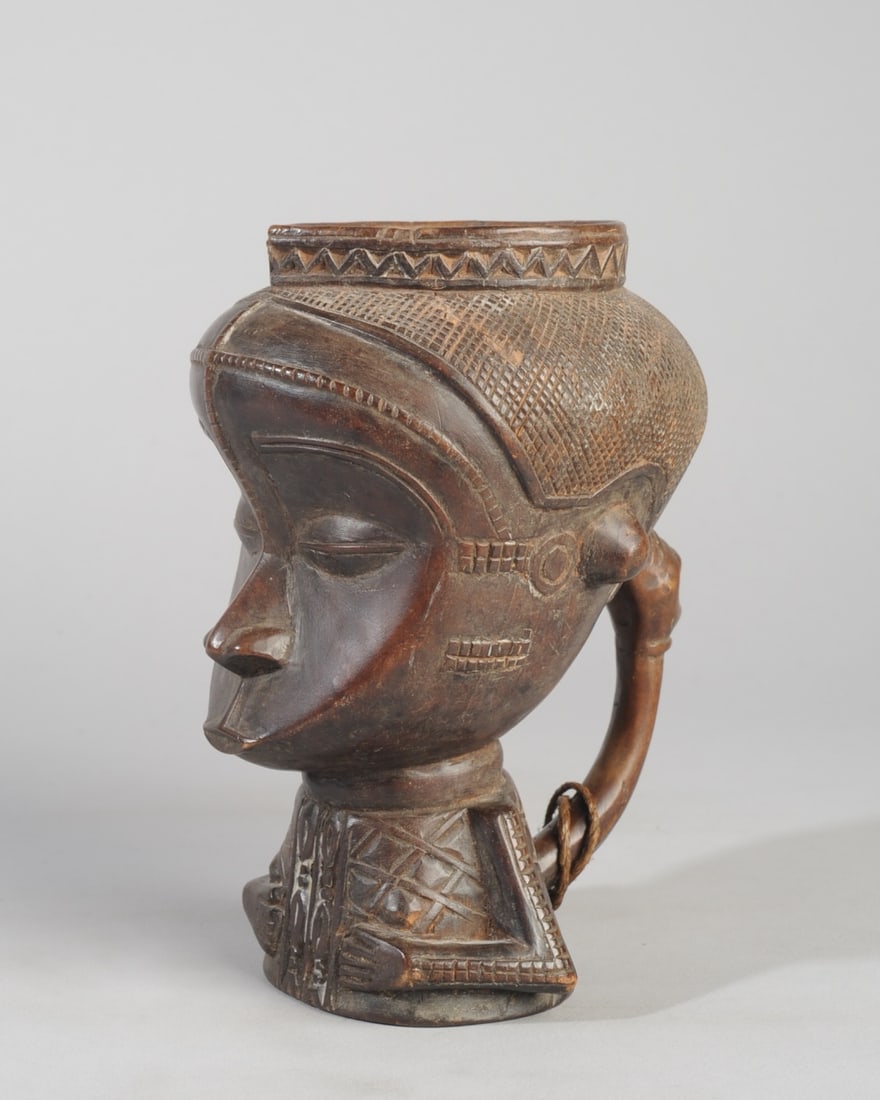 Kuba Palm Wine Cup, Ex-Zaire: Figurative palm wine vessel, the hollow upper part in the form of a head with concave, heart shaped face, coffee bean eyes under arched brows, naturalistic nose and small, pouting lips. With relief ca