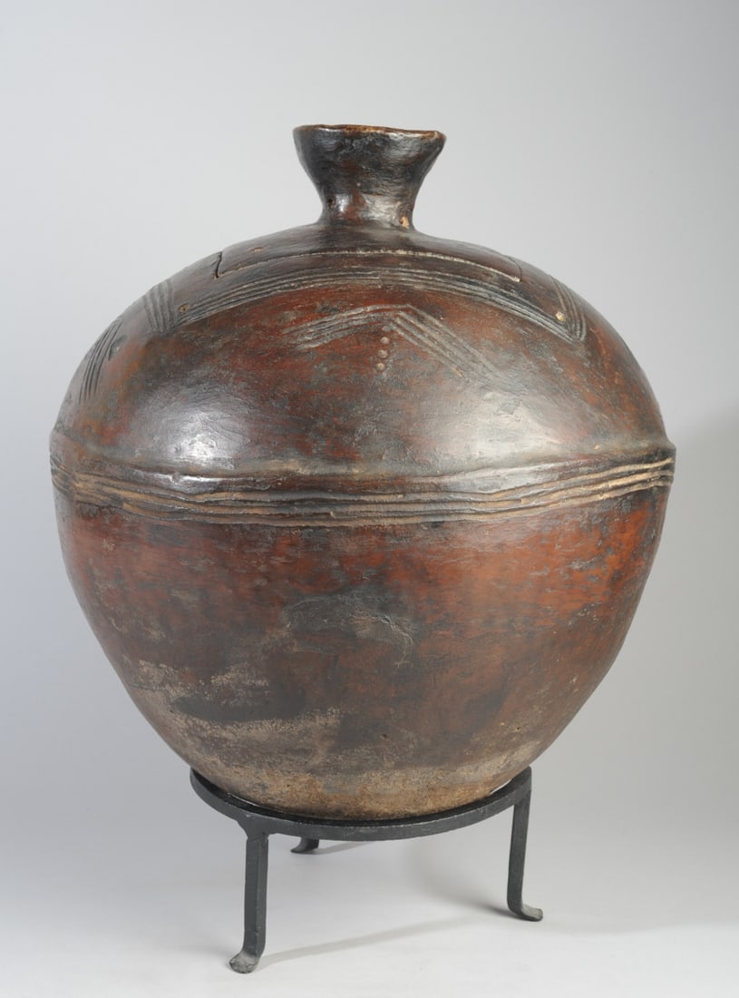 Lobi Lidded Pot, Burkina Faso: Round black terracotta pot, the lid with cup finial, the sides of the pot with incised linear decoration and relief bands to circumference, perhaps to make it easier to lift when full. On cast iron st
