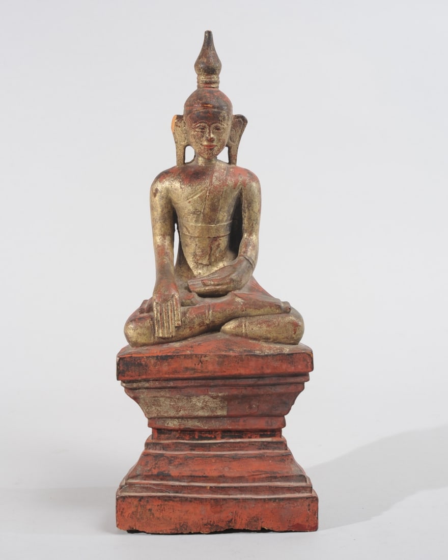 Antique Burmese Seated Gilt Wood Buddha: Gently smiling Buddha seated atop tall, waisted platform. Carved hardwood with red lacquer and gilt. Chip to top of one ear, possible loss to very tip of crown. Approx. 14 3/4" H. (37.4 cm)