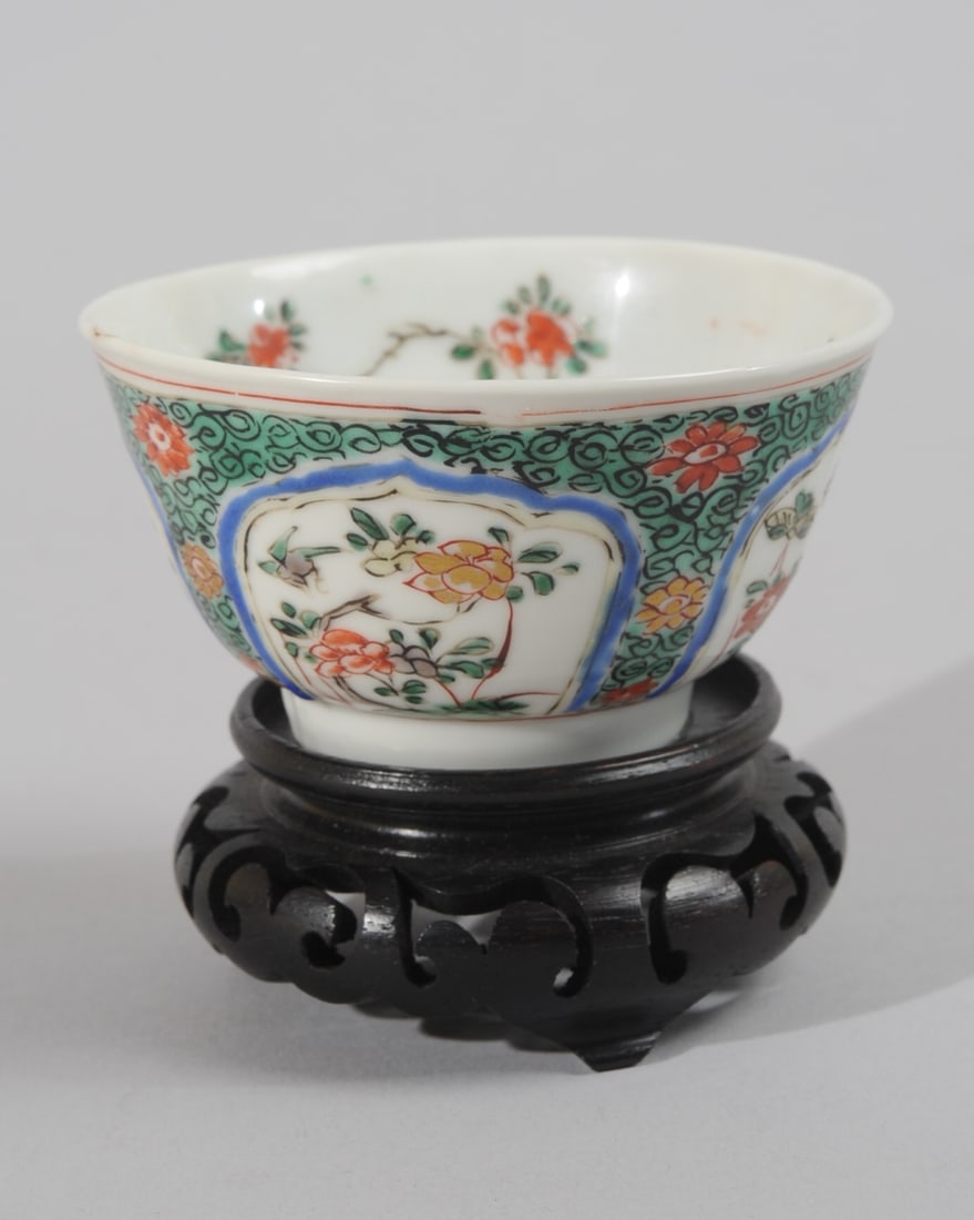 Chinese Kangxi Famille Verte Cup: Small tea cup, the sides with panels of flowers and butterflies against a green ground with scattered blossoms and black scrolling lines. Interior with scattered red blossoms around the sides and the