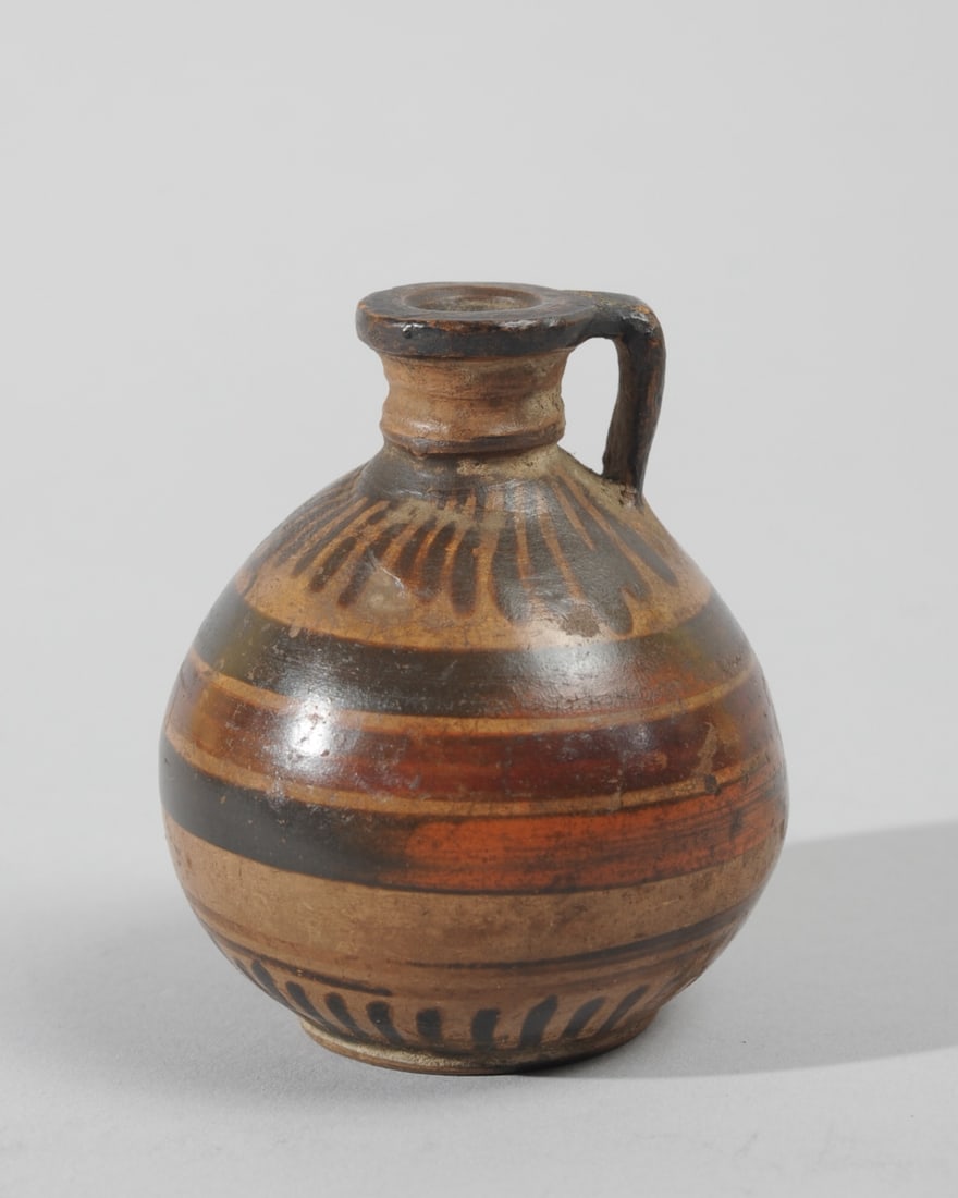Etrusco- Corinthian Aryballos: Archaic small terracotta oil flask with rounded body, narrow neck, flat rim, with loop handle from rim to shoulder, and with dark red and brown vertical and horizontal linear decoration. Likely Etrusc