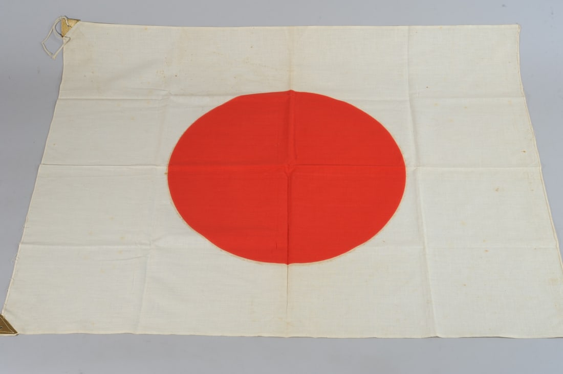 WW2 Japanese Flag: Cotton flag in red and white, with gold leather triangular reinforcements at holes for hanging. One set of ties intact. Minor foxing, minor old splashed rust colored stains, mostly washed or faded awa