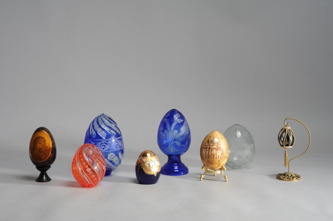 Mixed Egg Grouping: To include Murano glass egg, decorative blue glass egg, footed blue glass egg with double headed eagle, clear glass egg, red glass egg, miniature egg-form bird cage on stand, hand painted egg with nob