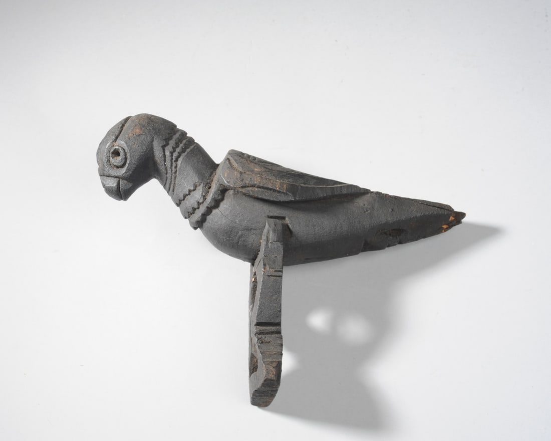 Timor Granary Rooftop Carved Bird Indonesia: ITIM/5Bird. 10” (25 cm) long body, 7” (17.5 cm) high including a separate piece of black wood for his legs/stand. Wood, black patina. Wings carved in geometric pattern. Carving of a bird, 