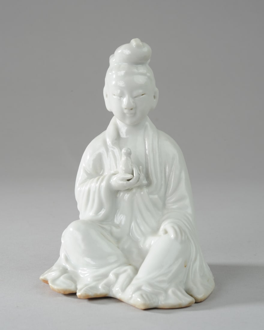 Chinese Blanc de Chine Guanyin Figure: Seated late Qing / Republic period porcelain figure of Guanyin, goddess of compassion, shown holding her jar of pure water. Unglazed base with impressed manufacturer's mark within diamond shape and wi