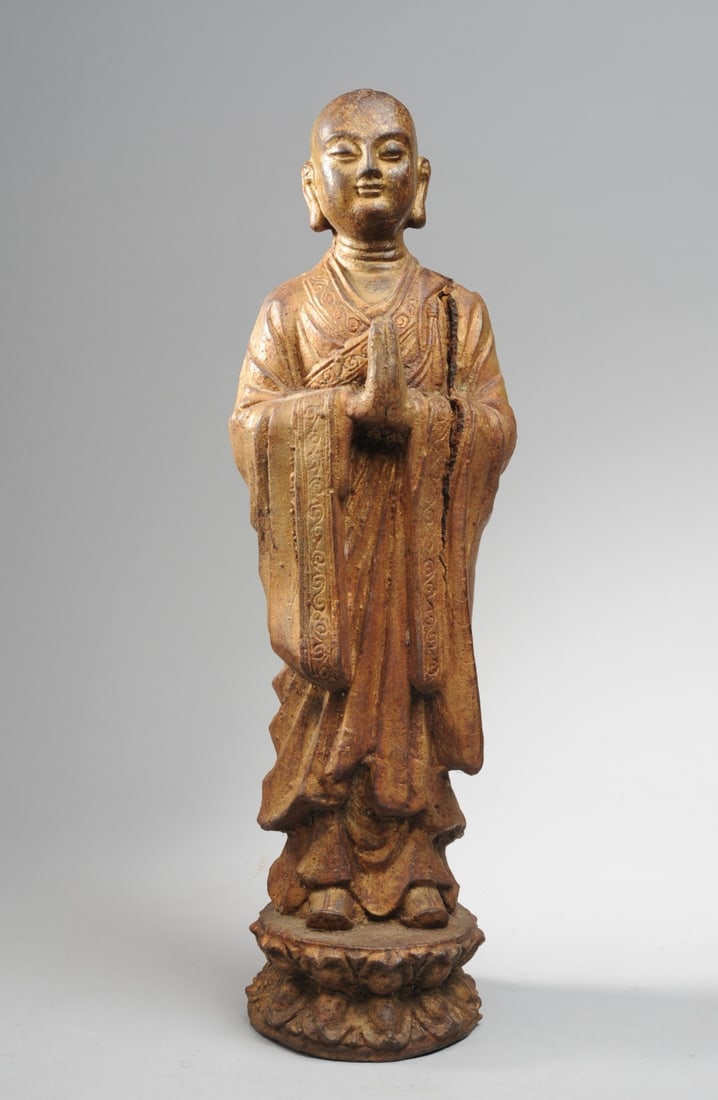 Antique Chinese Cast Iron Buddha or Lohan: Standing figure of Lohan or Buddha with palms together, feet resting on lotus base. Traces of original gilt. Large crack from behind left ear to 2/3 length of sleeve. Very heavy. Approx. 19 3/4" H. Se