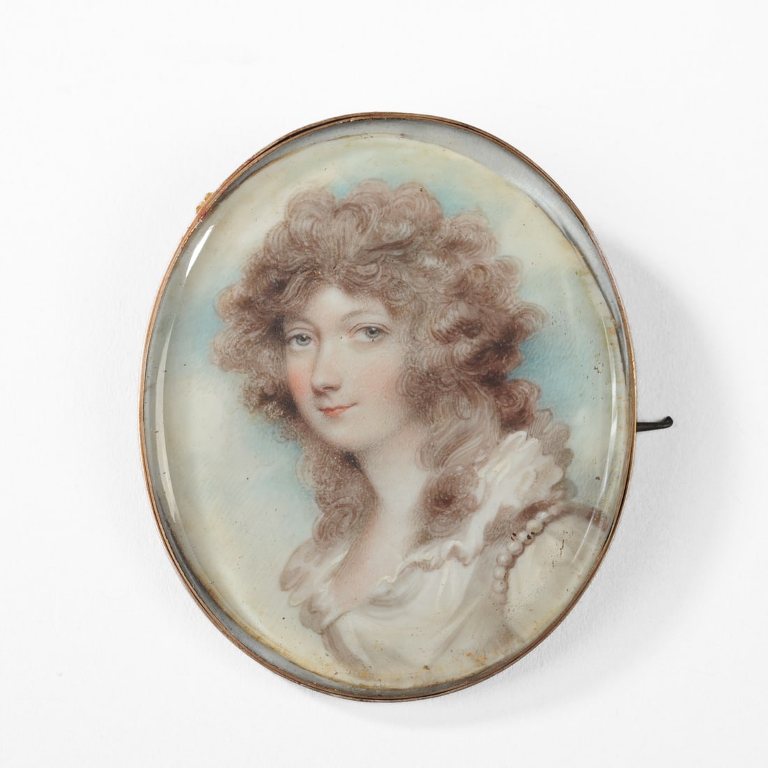 Portrait Miniature of a Lady: Oval miniature of a striking young woman with voluminous curly hair, dressed in a white gown with pearl adornment. Late 18th / early 19th century. Approx. 2 1/4" x 2". Provenance: By descent in the Ve