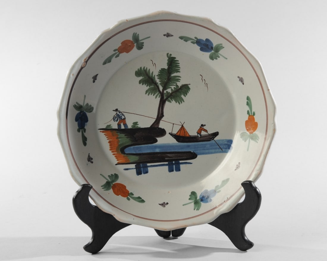 French Faience Plate: Barbed rim. Central decoration of a man in a boat pulled by another on the shore. Floral rim. Likely Nevers faience. No chips, cracks, or repairs. Expected glaze skips. Approx. 9" D. Our primary recom
