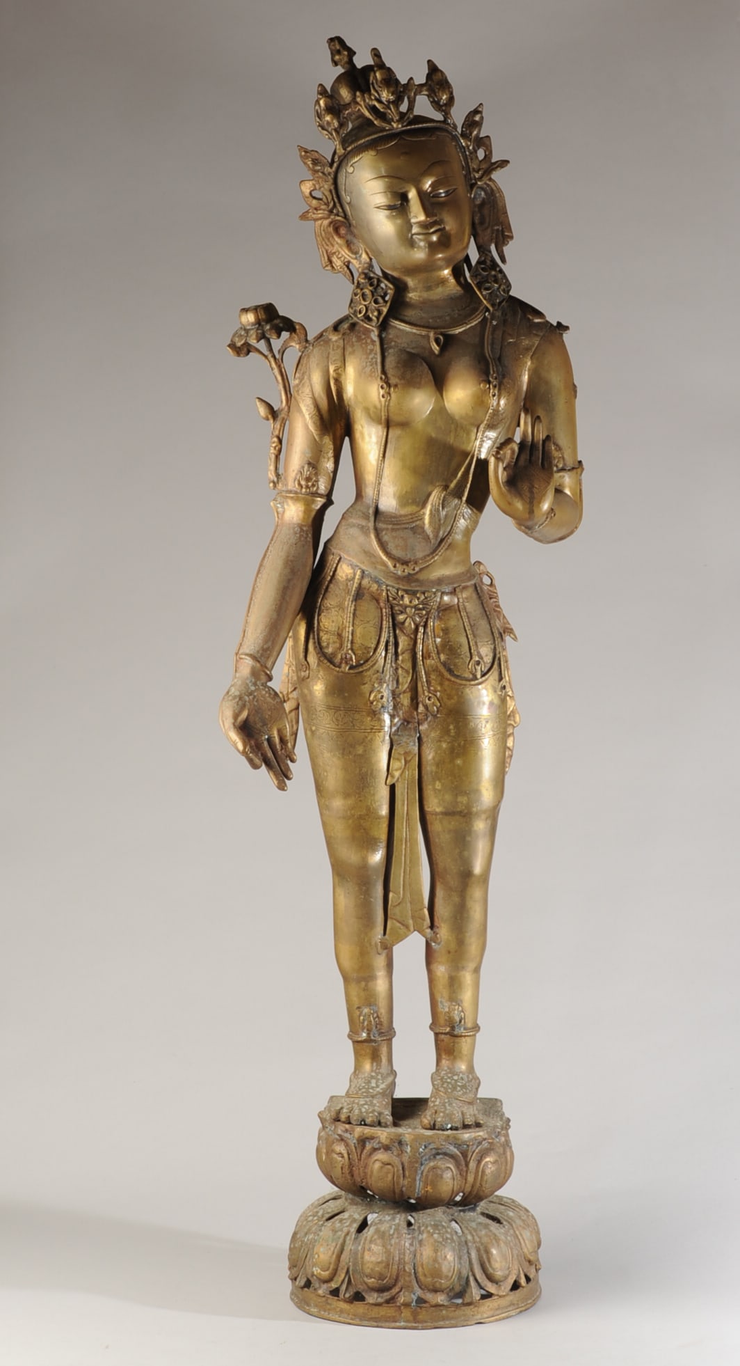 50" Nepalese Brass Alloy Figure of Green Tara: Large mid-20th C. Newar-style Nepalese brass alloy figure of Green Tara, depicted standing on a lotus base and wearing a floral crown. Lotus stalks bloom at each shoulder. Her right hand is held in Va