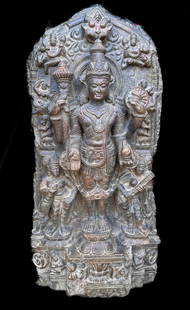 Nepalese Stone Temple Stele, Vishnu: Carved stone Pala-Newar style stele depicting four-armed Vishnu standing on double lotus pedestal and flanked by attendants and celestial beings. Figure is carved within an architectural arch. Dark,
