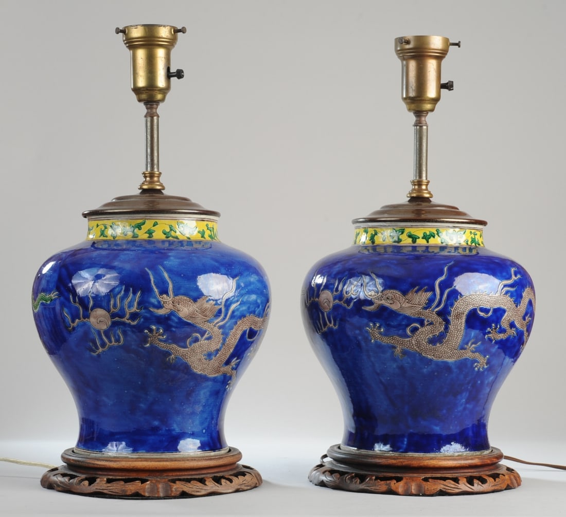 Pair Chinese Porcelain Dragon Jars, Lamped: Substantial porcelain jars with green, five-toed dragons and a flaming pearl on a washy, deep cobalt blue ground, with yellow-ground band at neck with green vines. Carved wood bases and brass fittings