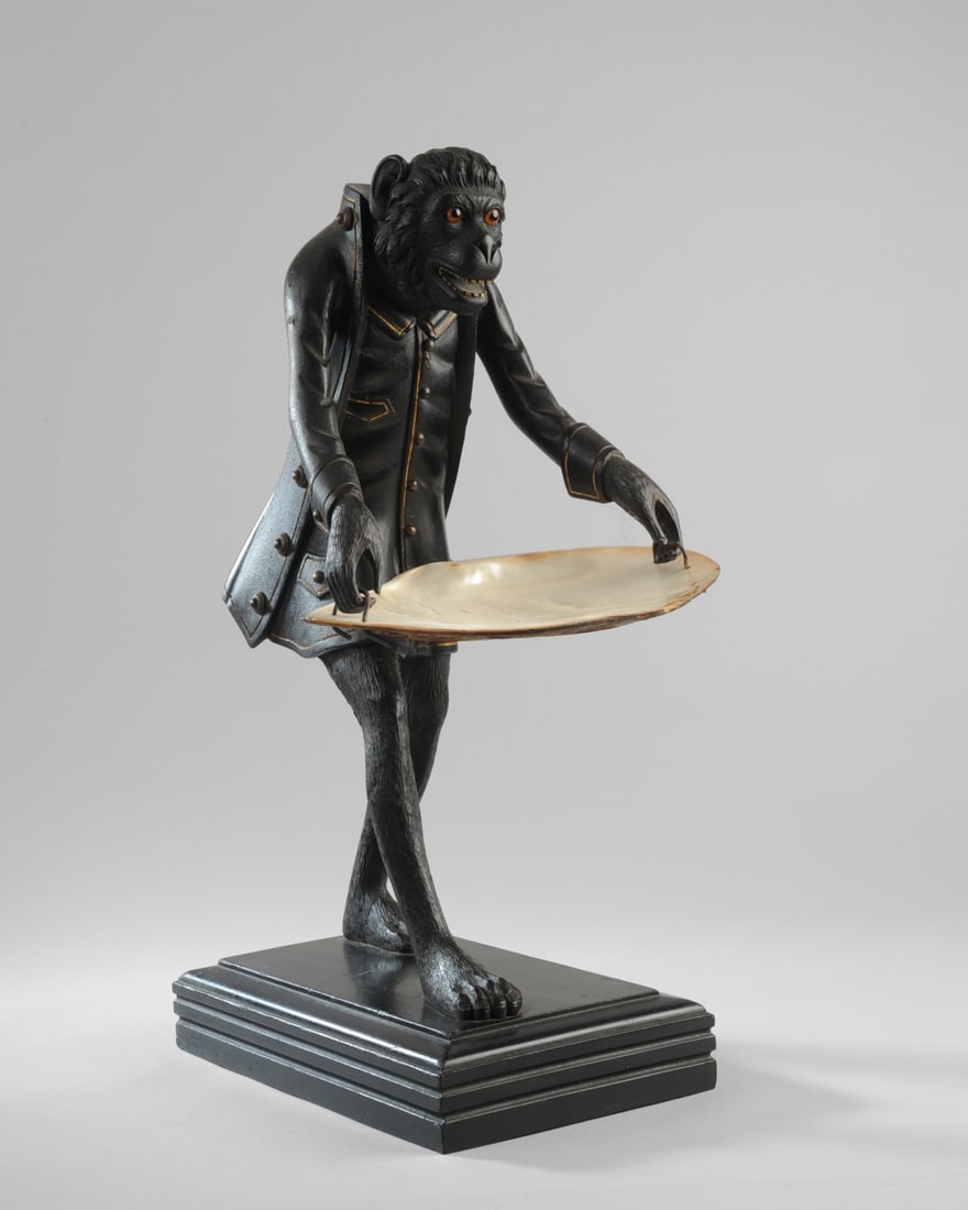 Antique Monkey Butler Figure w/ Shell Tray: Carved hardwood striding figure of a monkey in 18th C. butler's jacket, carrying a large natural shell as a tray. Mouth is open to reveal square carved teeth. Glass eyes. Original carved hardwood base